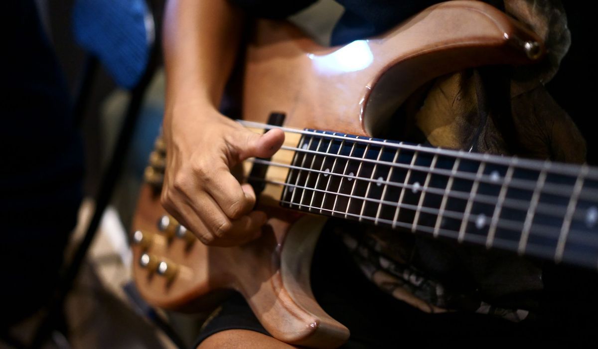 Player fretting a wooden electric bass