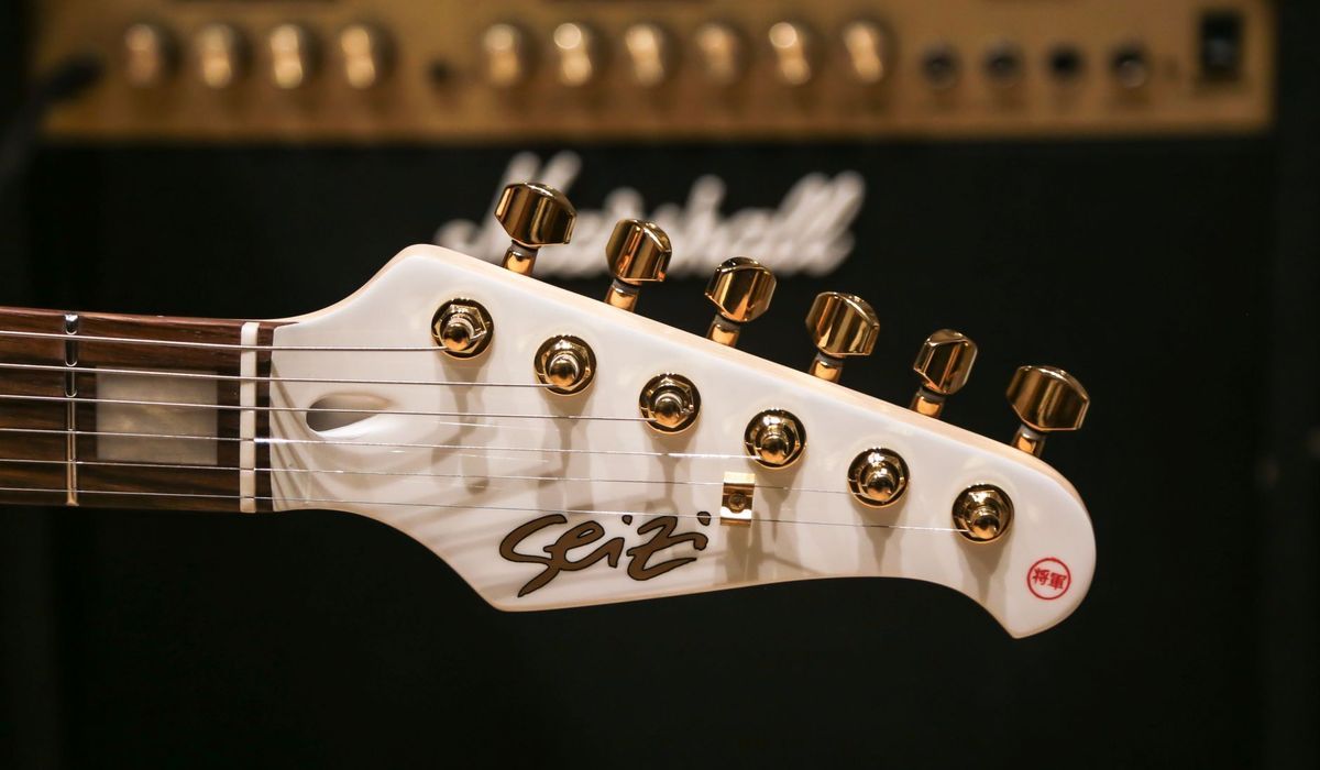 White electric guitar headstock in front of an amp
